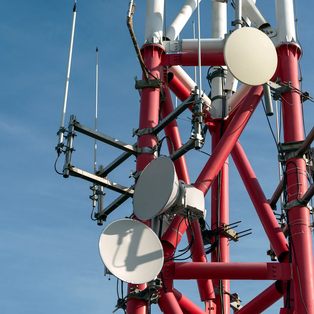 Close-up of a red and white telecommunications tower with multiple round and rectangular antennas against a clear blue sky.