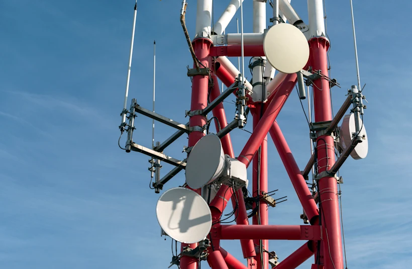 Close-up of a red and white telecommunications tower with multiple round and rectangular antennas against a clear blue sky.