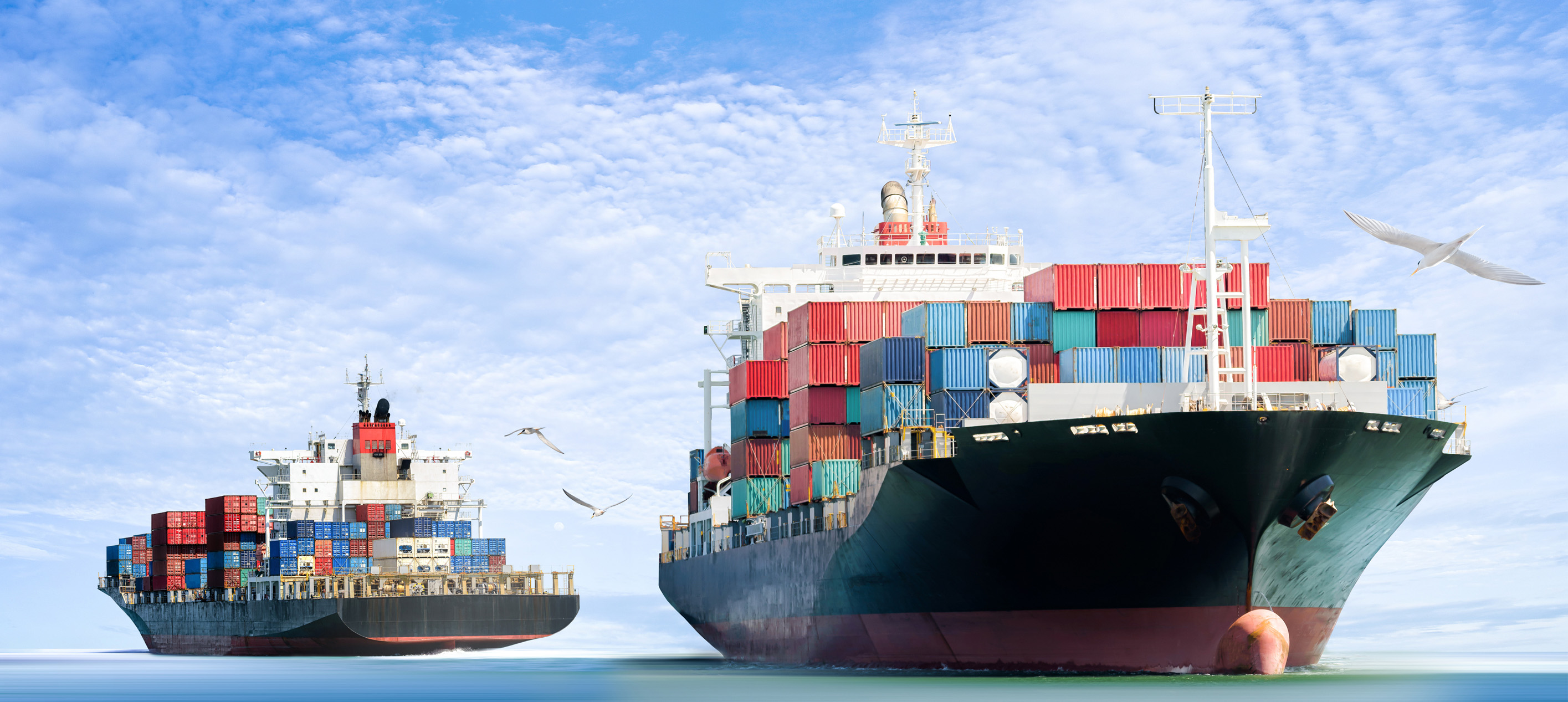 Two cargo ships carrying colorful shipping containers sail across the sea under a blue, cloudy sky, illustrating global trade and maritime transport.