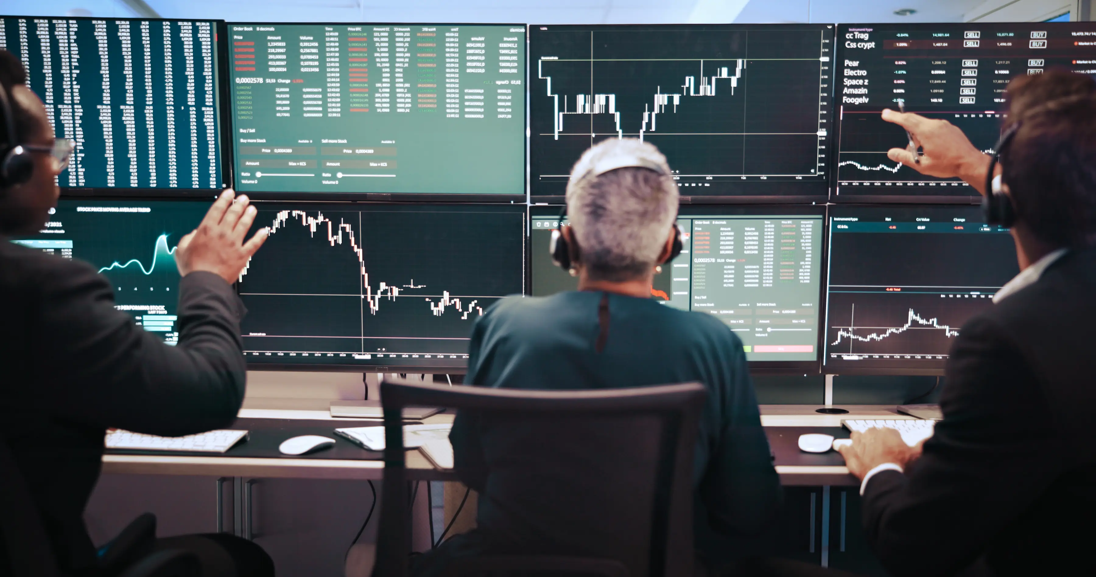Three people wearing headsets monitor large screens displaying stock market charts and data in a trading room.