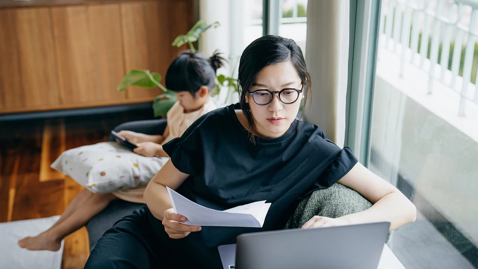 Mastering money management - Mother looking at her laptop while her daughter is on her tablet