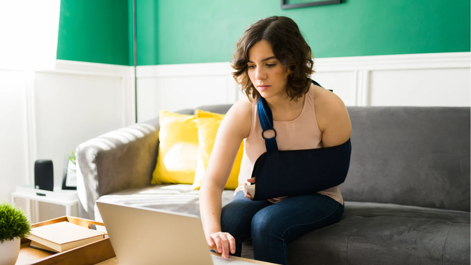 Young woman with arm sling using a laptop