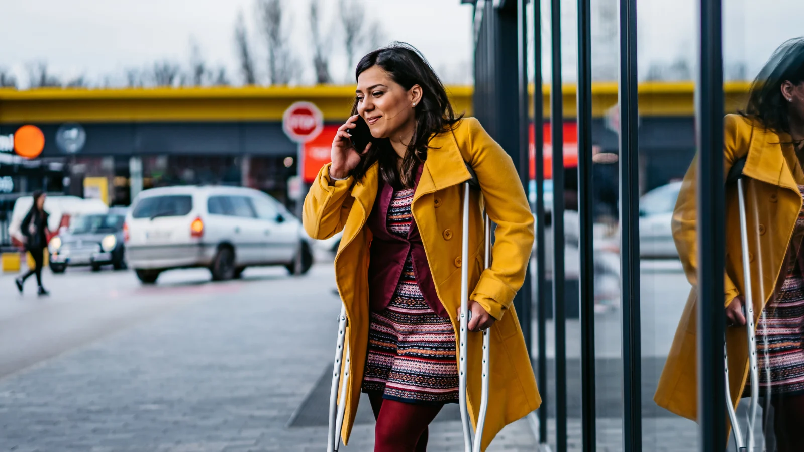 Young woman holding crutches while talking on a phone outside