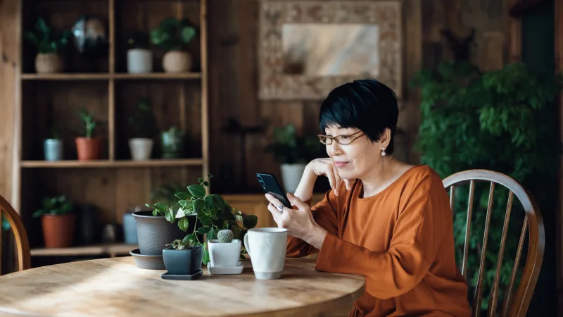 Woman reviewing cost comparisons on mobile phone at kitchen table