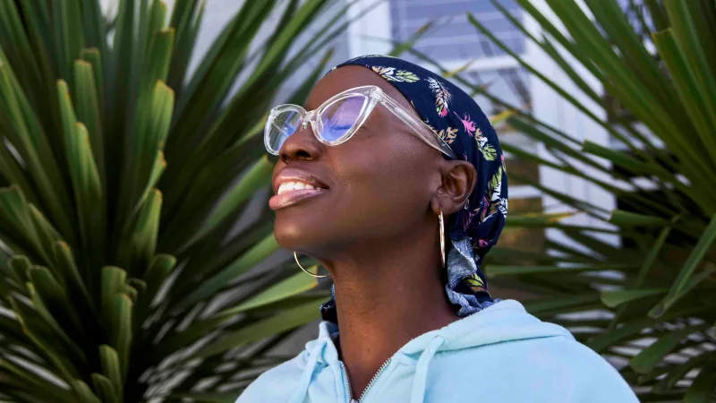 A woman with a head scarf and sunglasses tilts her face toward the sun