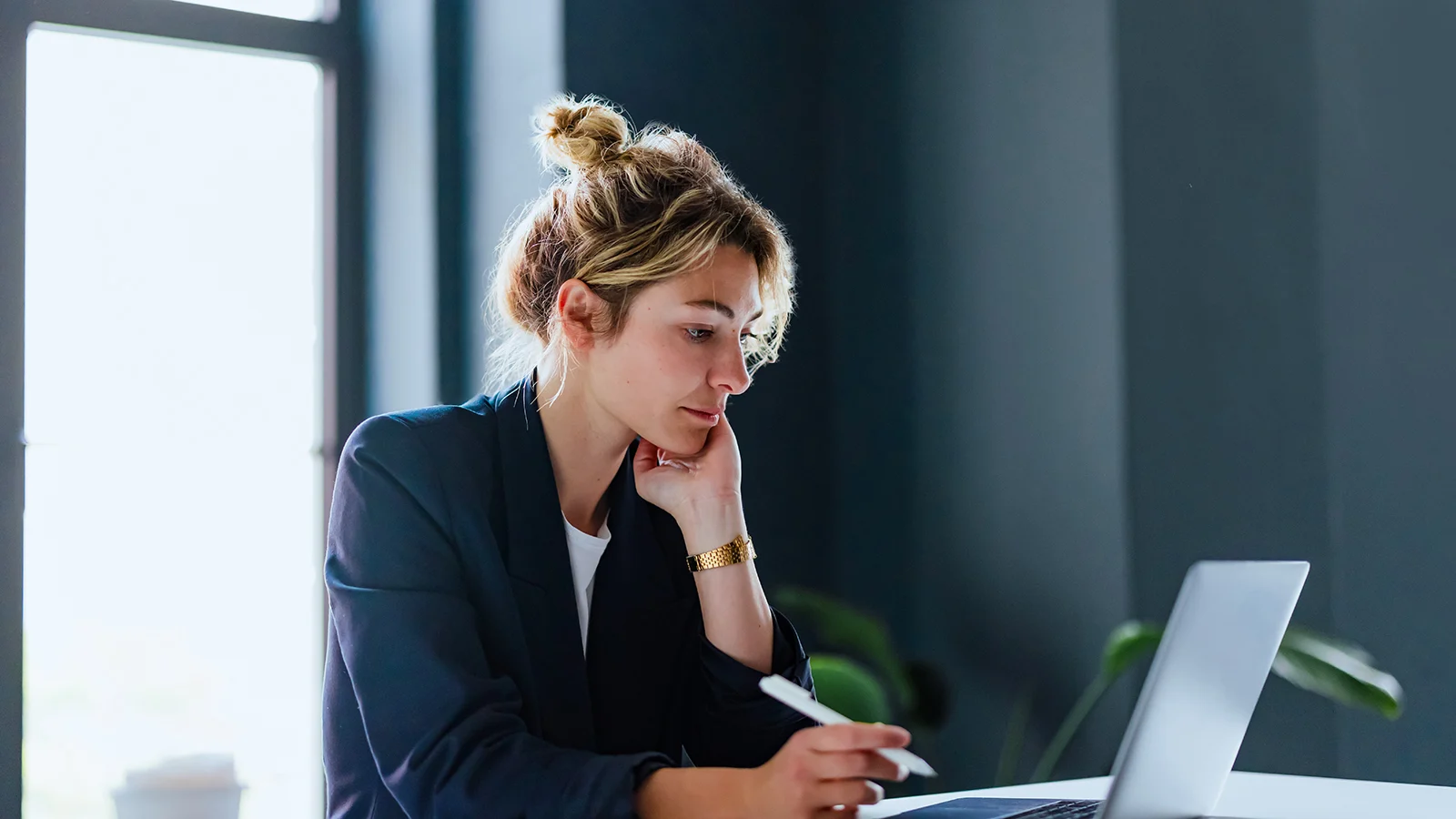 Person working on a laptop at a desk in a modern office, holding a stylus and looking at the screen.