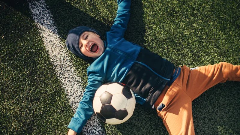 How supplemental health insurance works - Young boy playing soccer and laying down in grass with soccer ball