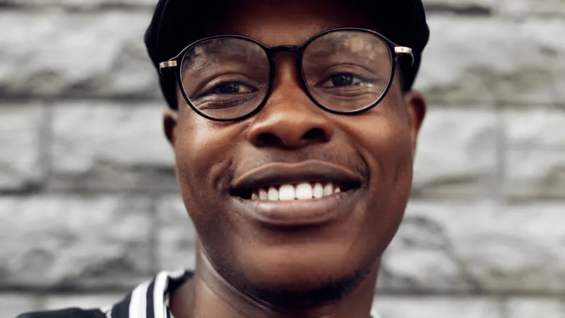 How to support employee health and well-being, one smile at a time - Smiling man in front of brick wall