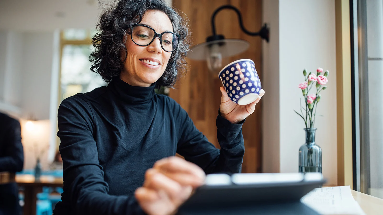 Person holding a coffee mug while working on a tablet at a table.