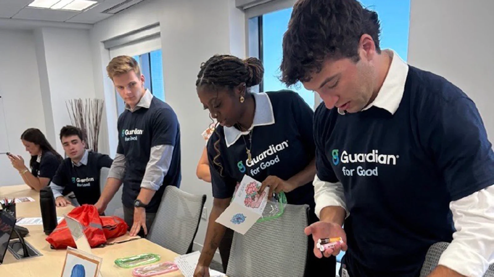 People wearing Guardian for Good shirts work together on a volunteer activity around a conference table.