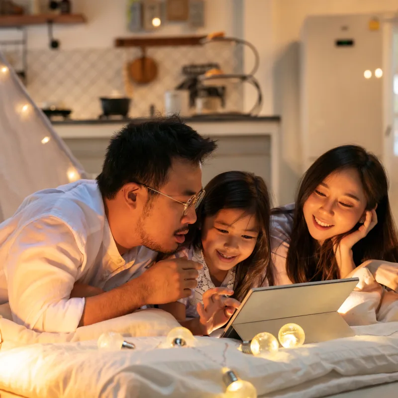 A mom, dad, and daughter, read a book on pillows on the floor