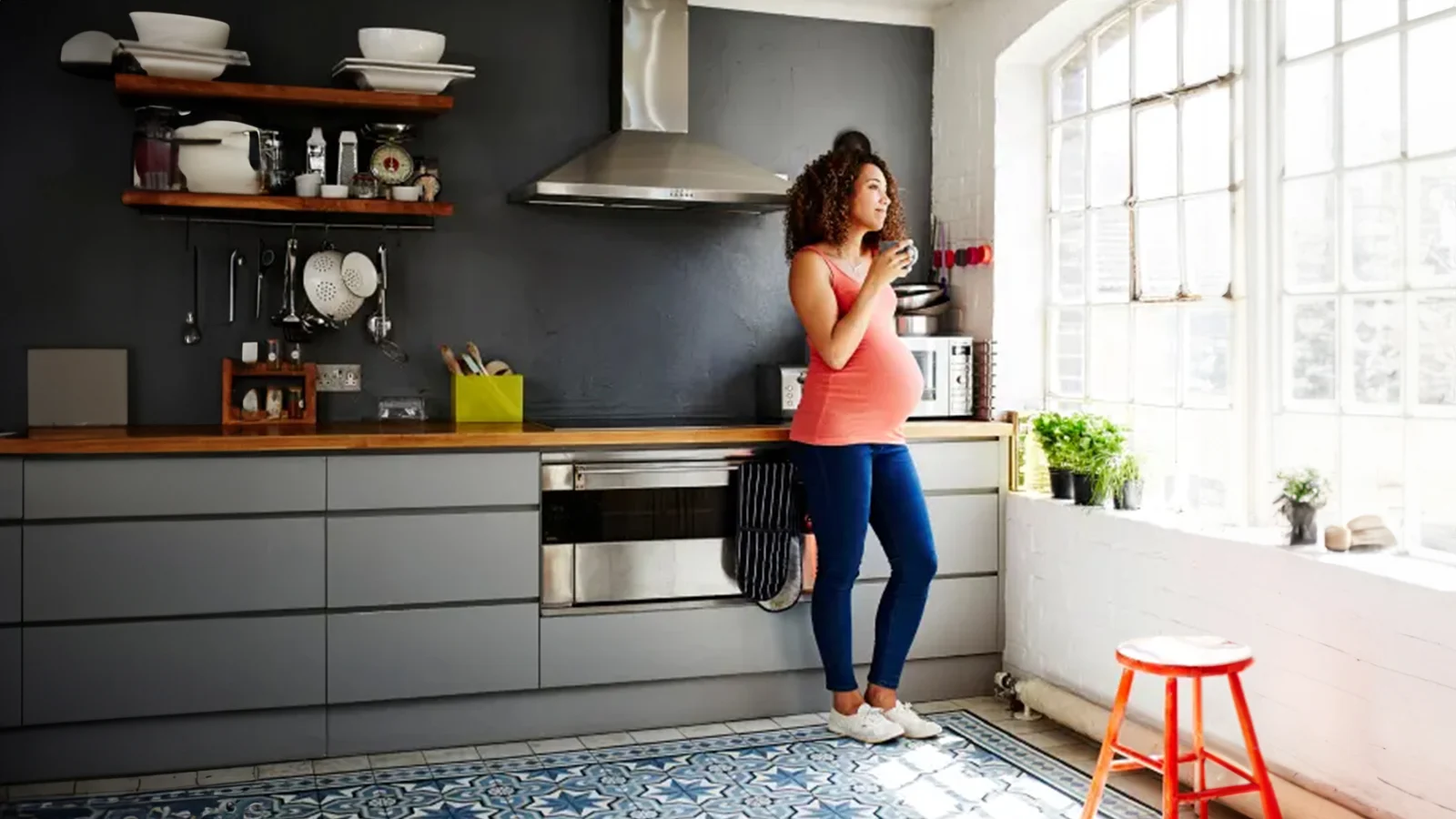 How to create a budget - Pregnant woman drinking coffee and looking out of kitchen window.