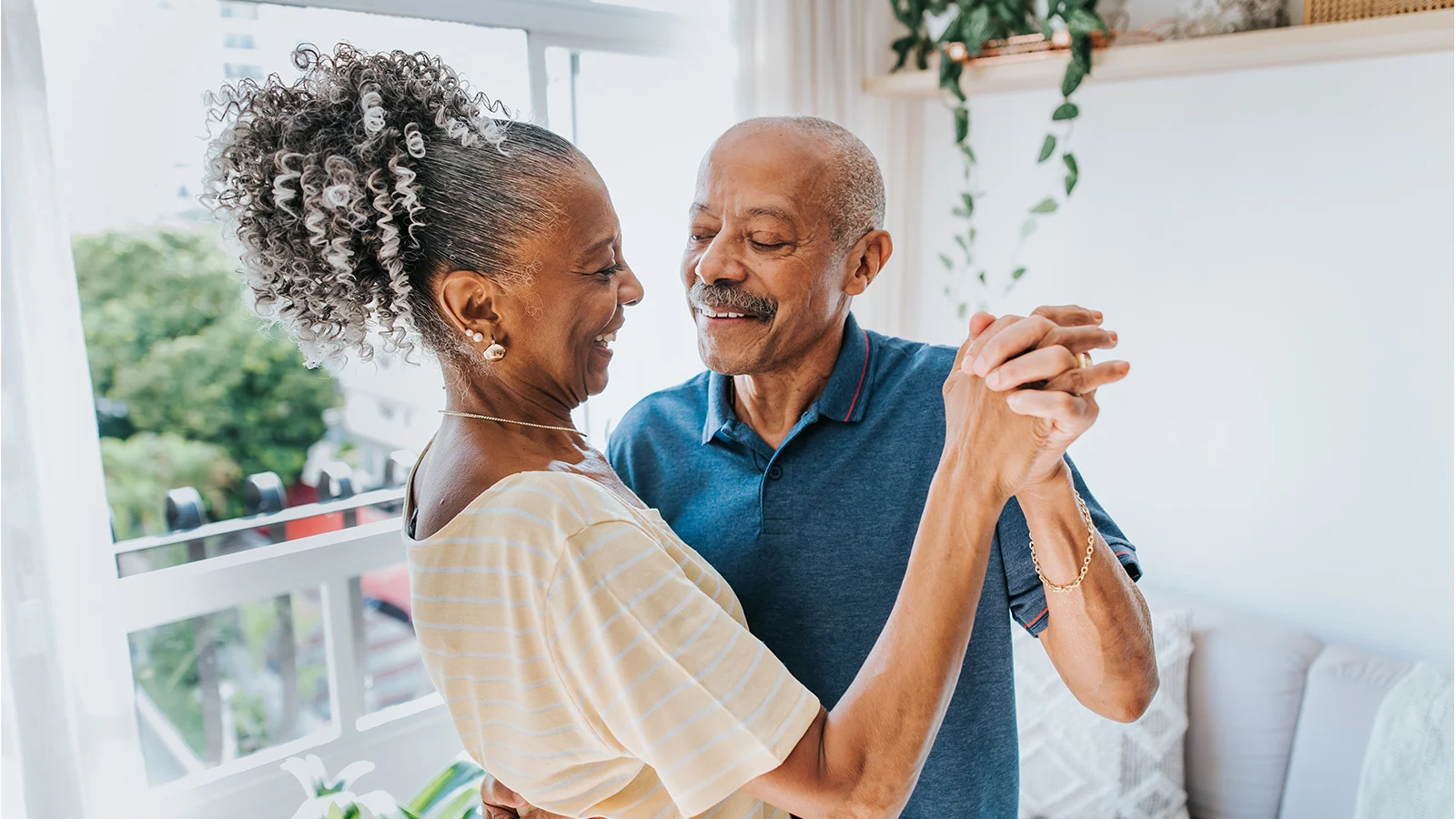 Senior couple dancing together in a sunlit living room at home.