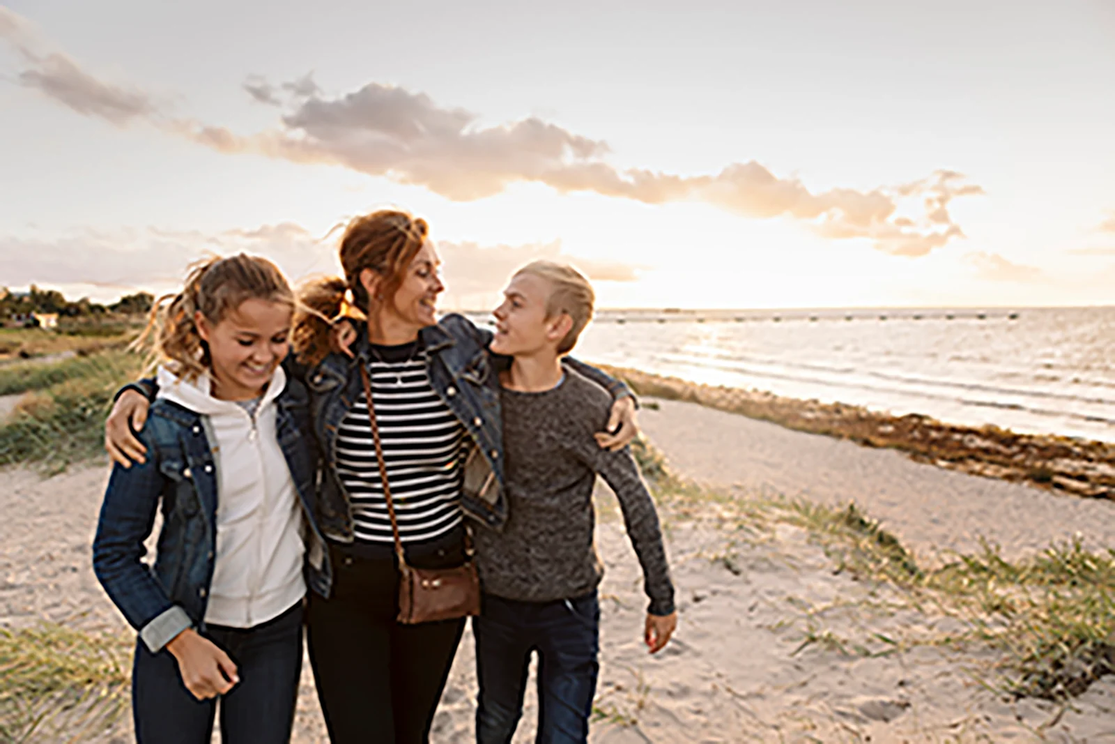 Mother and her two preteen children walking on the beach.