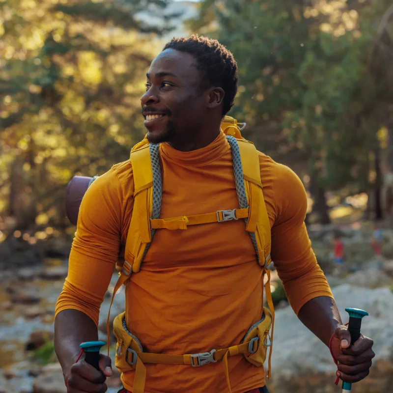 A man hikes in the woods with an orange backpack