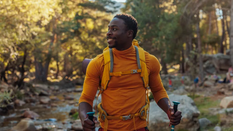 Addressing every aspect of  well-being - A man hikes in the woods with an orange backpack