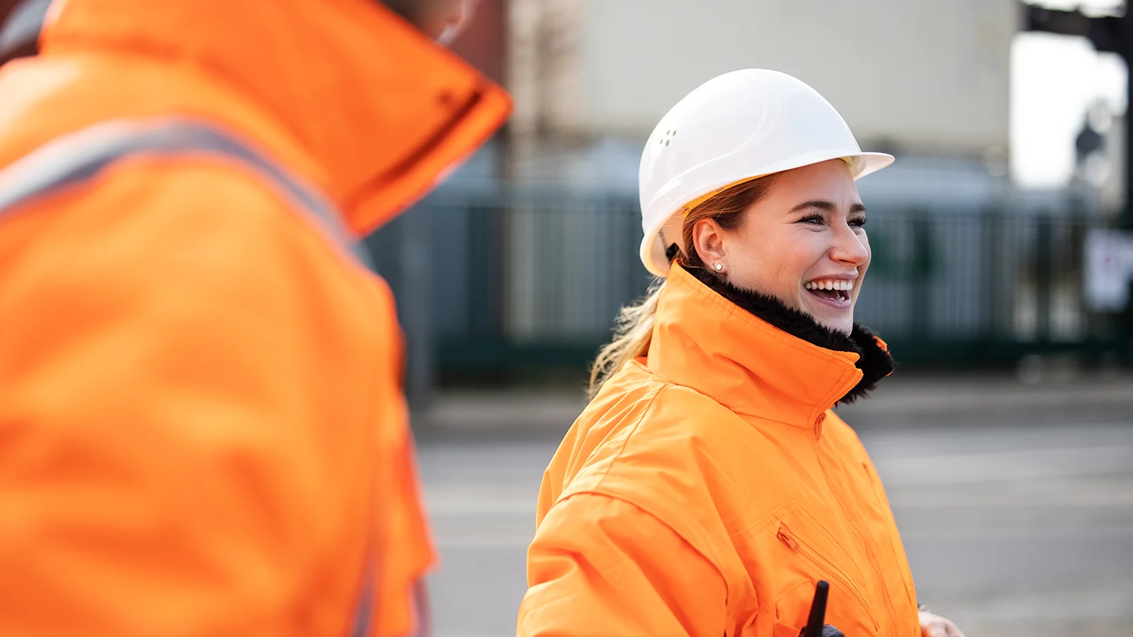 Woman in bright orange jacket wearing a construction hat smiling