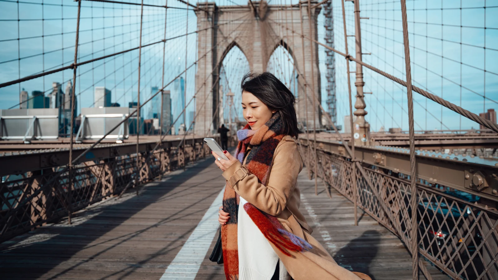 Woman looking at mobile phone and smiling on Brooklyn Bridge