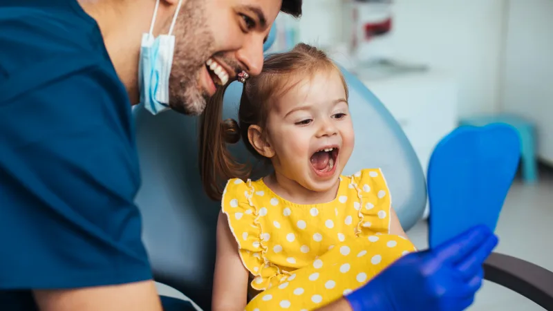 We help our community’s most vulnerable residents restore their confidence and their smiles by providing access to the dental care they need - A dentist wearing a mask and gloves examines a patient’s mouth