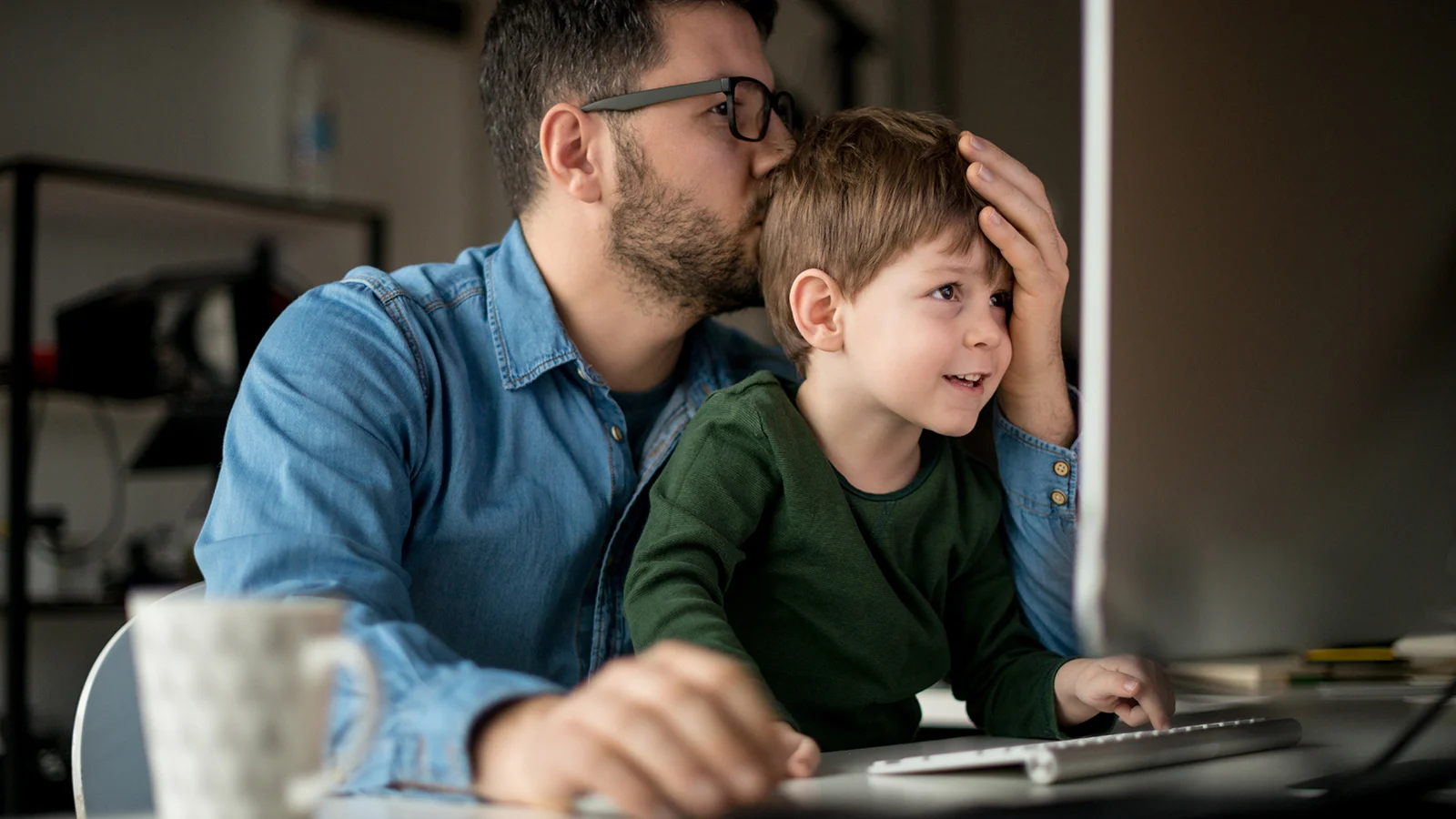 Father working on a computer with his young son sitting on his lap.