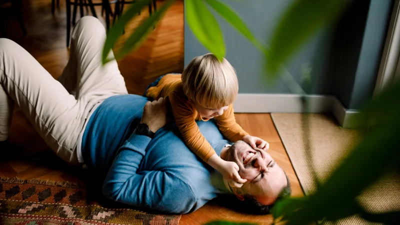 5 ways for single parents to improve their finances and overall well-being - Single father happily playing with young child on living room floor