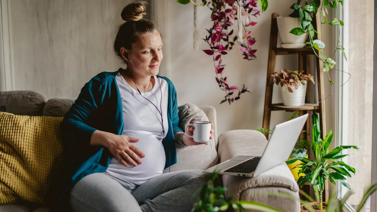 Pregnant person using a laptop at home, representing pregnancy health and wellness.