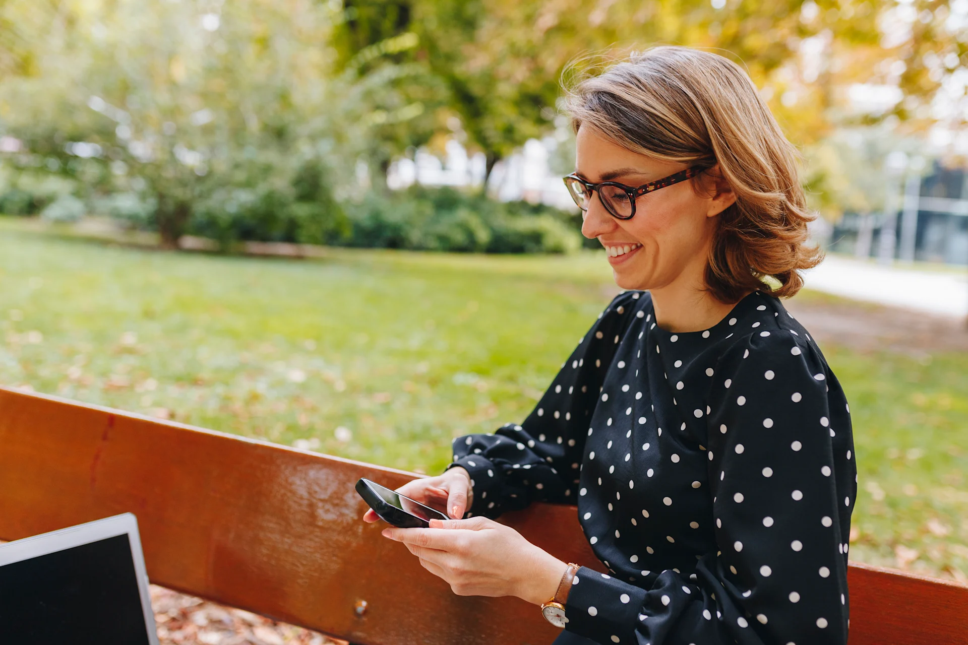 Smiling woman freelancer text messaging through smart phone in public park