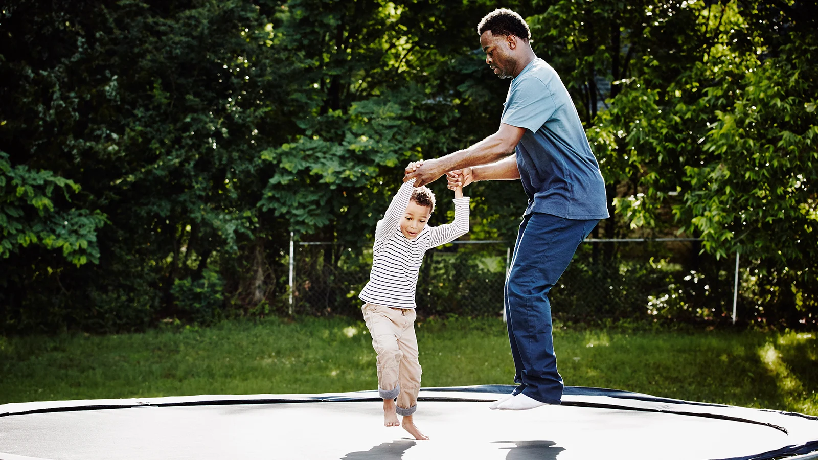 Father holding his sons hands jumping on a trampoline