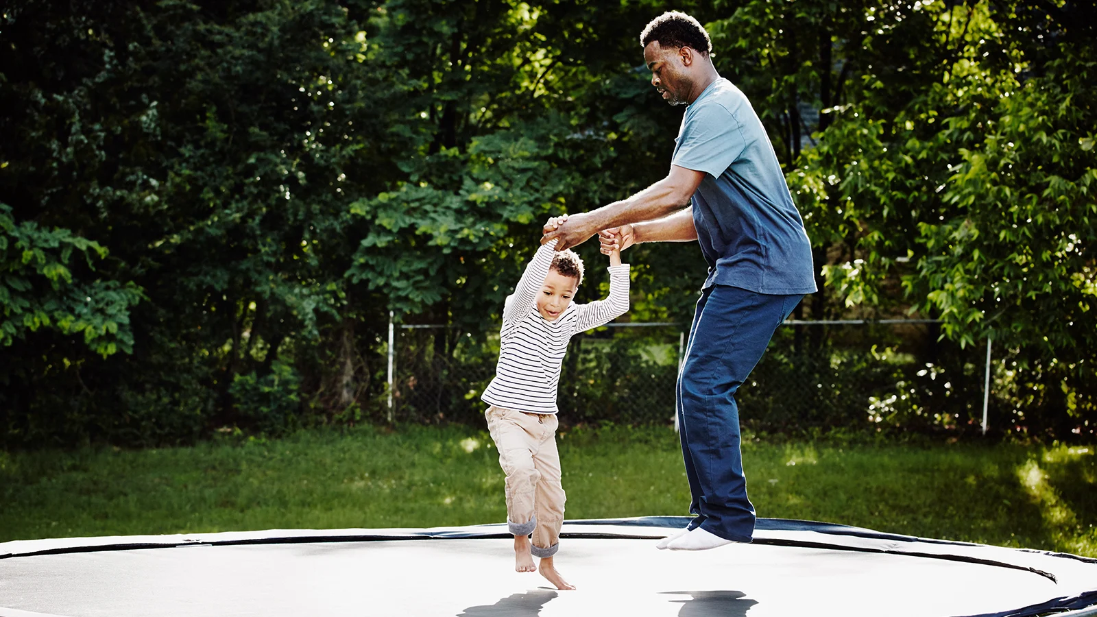 Supplemental health plans at work  - Father holding his sons hands jumping on a trampoline