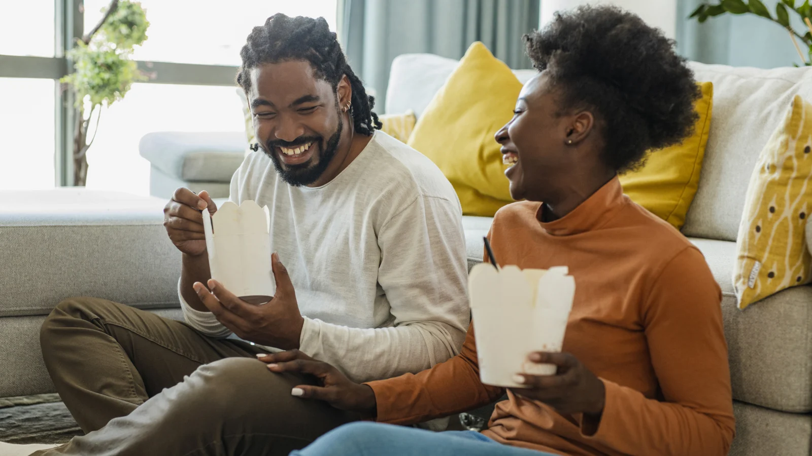 Couple laughing together while eating takeout food.
