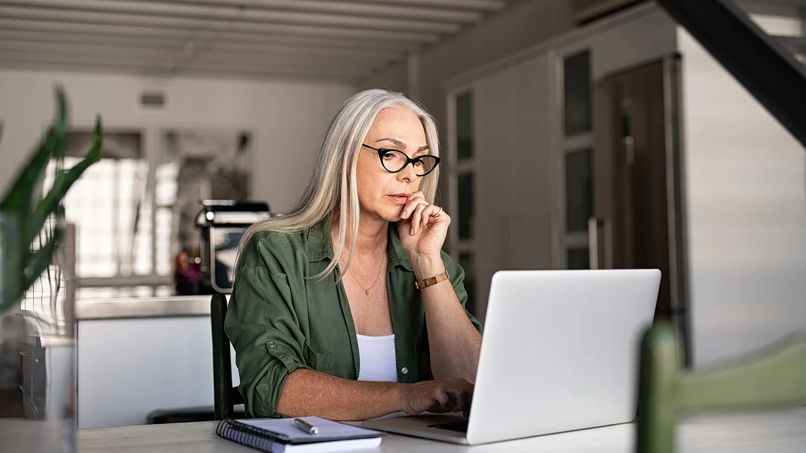 Person using a laptop at a desk in a home office with a notebook nearby