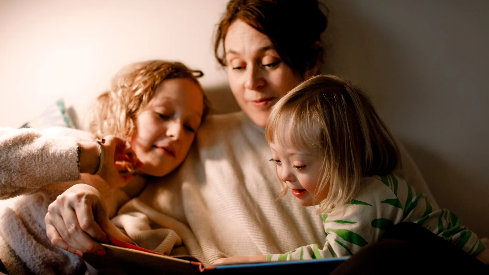 Girl with down syndrome reading a book with her mother and sister