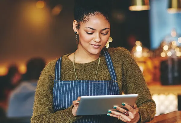 woman standing in her cafe looking at a tablet