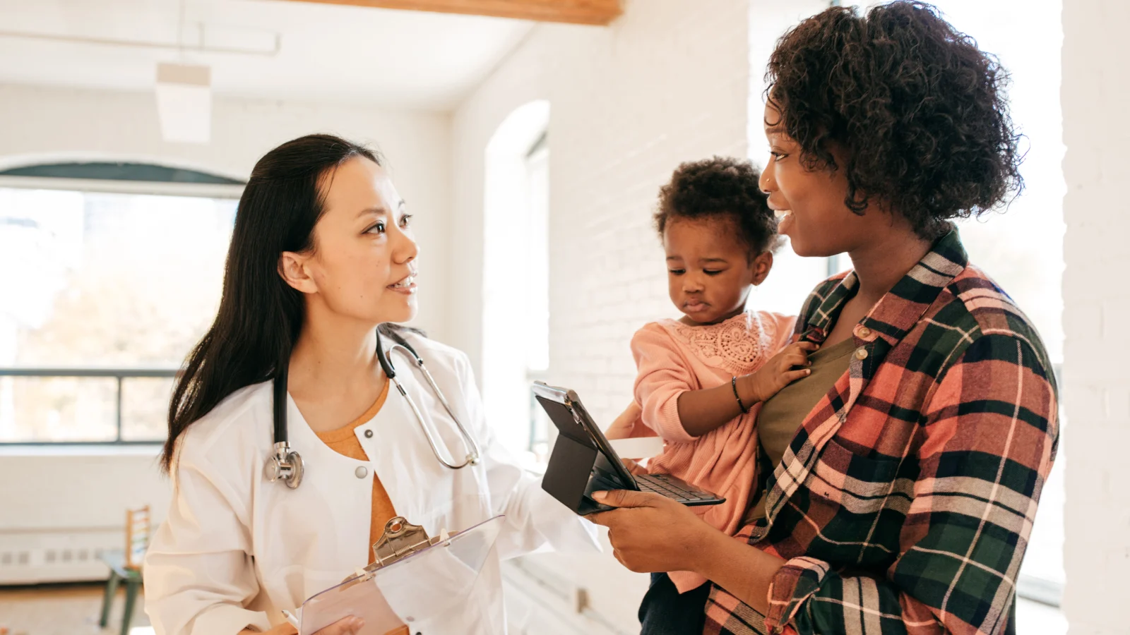 Woman holding her child and speaking with her physician.