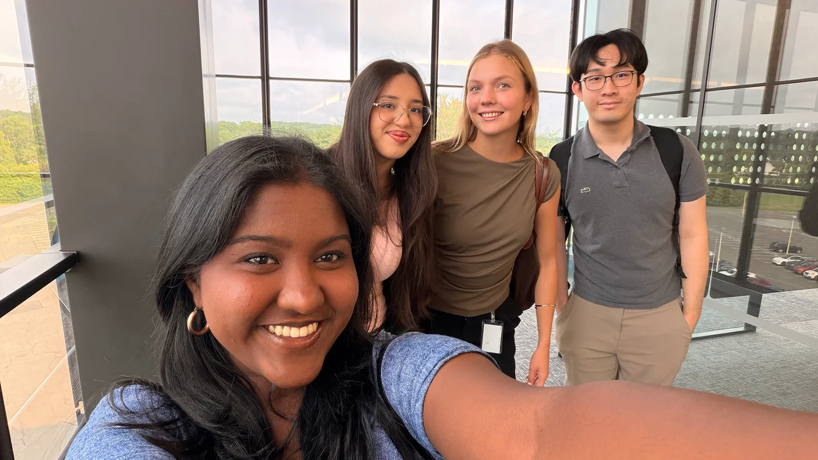 Four people pose for a group selfie in a bright office with floor-to-ceiling windows.
