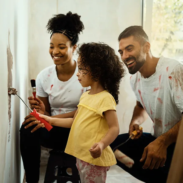 Mother and father painting a wall with their daughter.