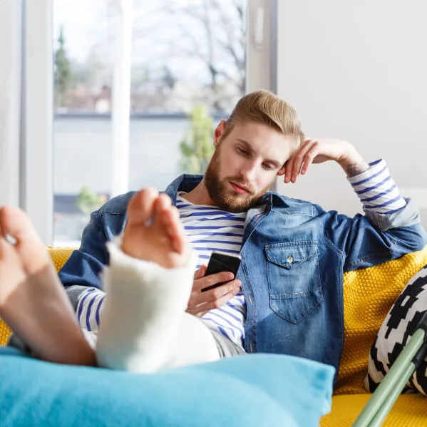 Man with a fractured leg looking at a phone.