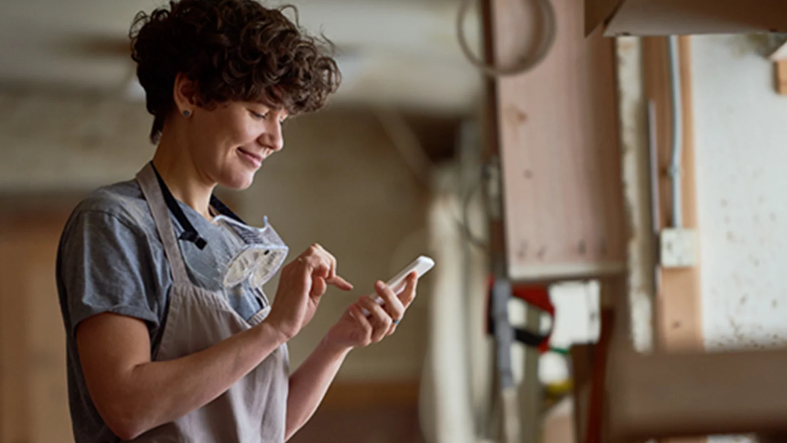 It’s time to make it alone and you’ve never been more excited!  - Woman standing in a workshop on her phone