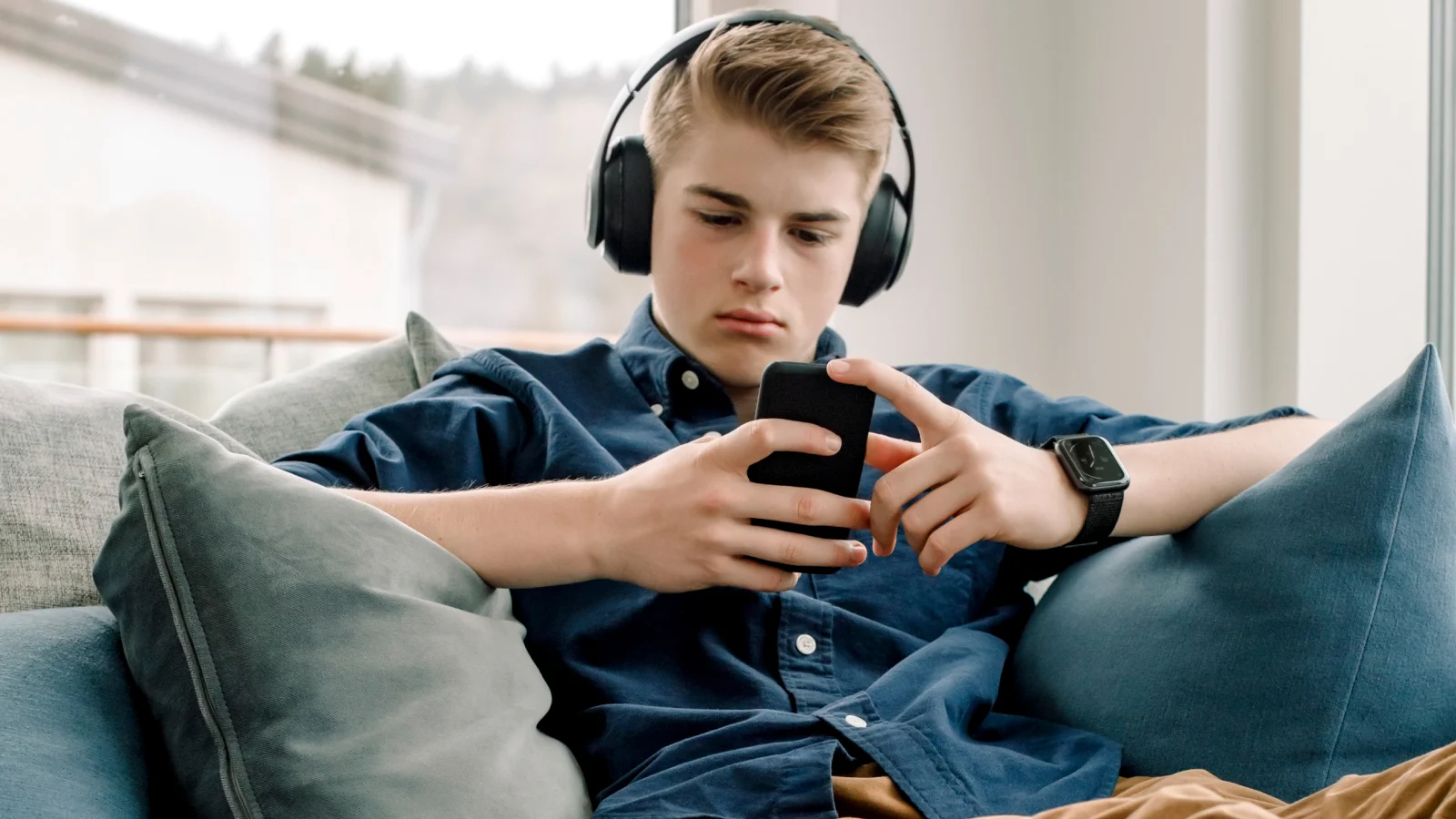 Focused on privacy - teen boy on couch with headphones on looking at phone