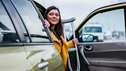 Woman getting out of her car carrying crutches