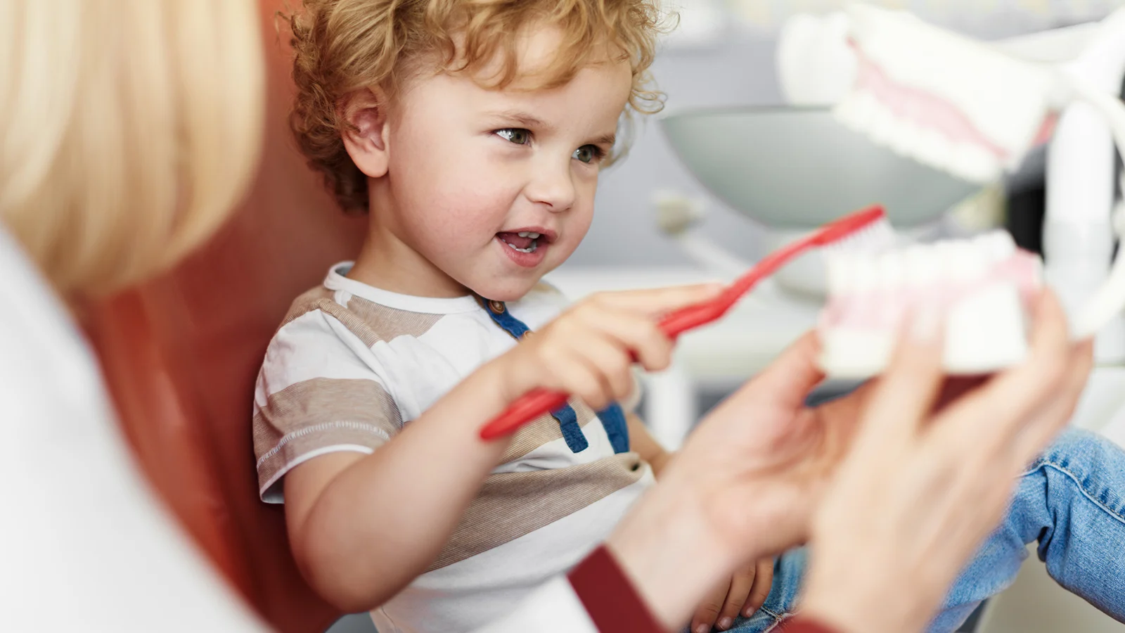 Dentist showing a little boy how to brush his teeth.
