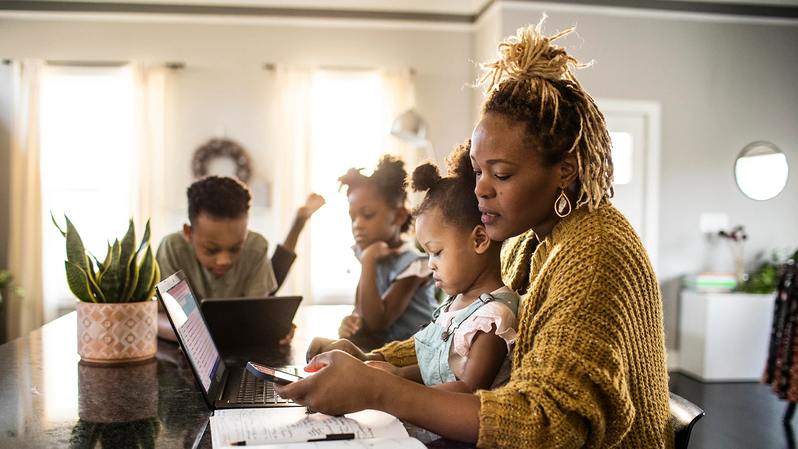 Parent holding a young child while working on a laptop at home