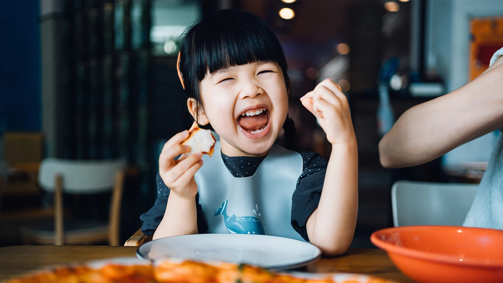 Happy little Asian girl enjoying pizza and smiling