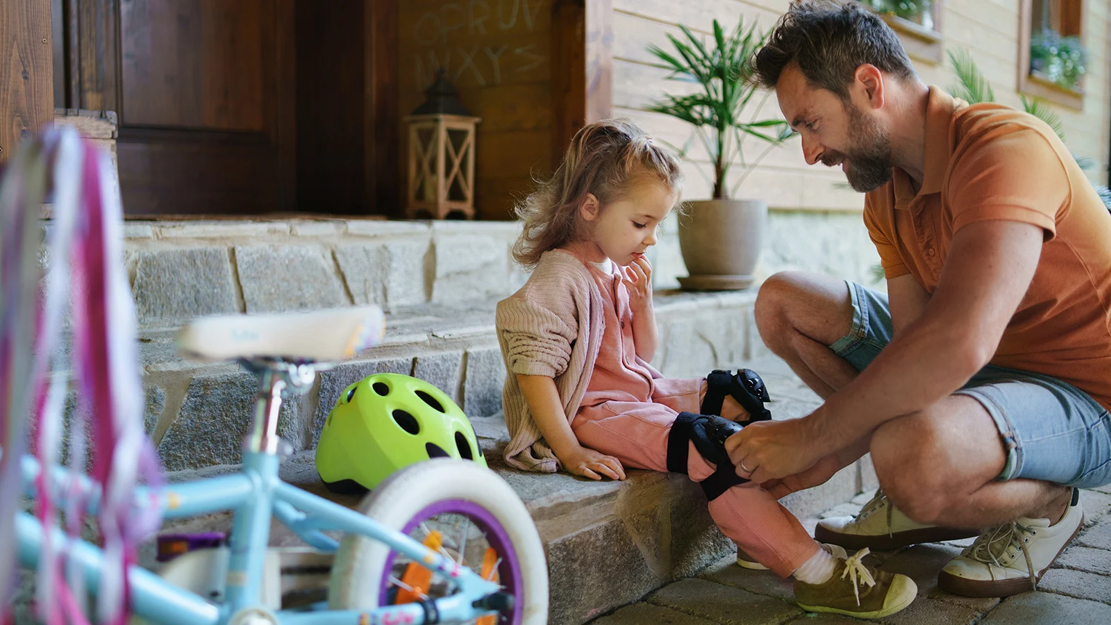 Father putting pads on daughter before she rides her bike