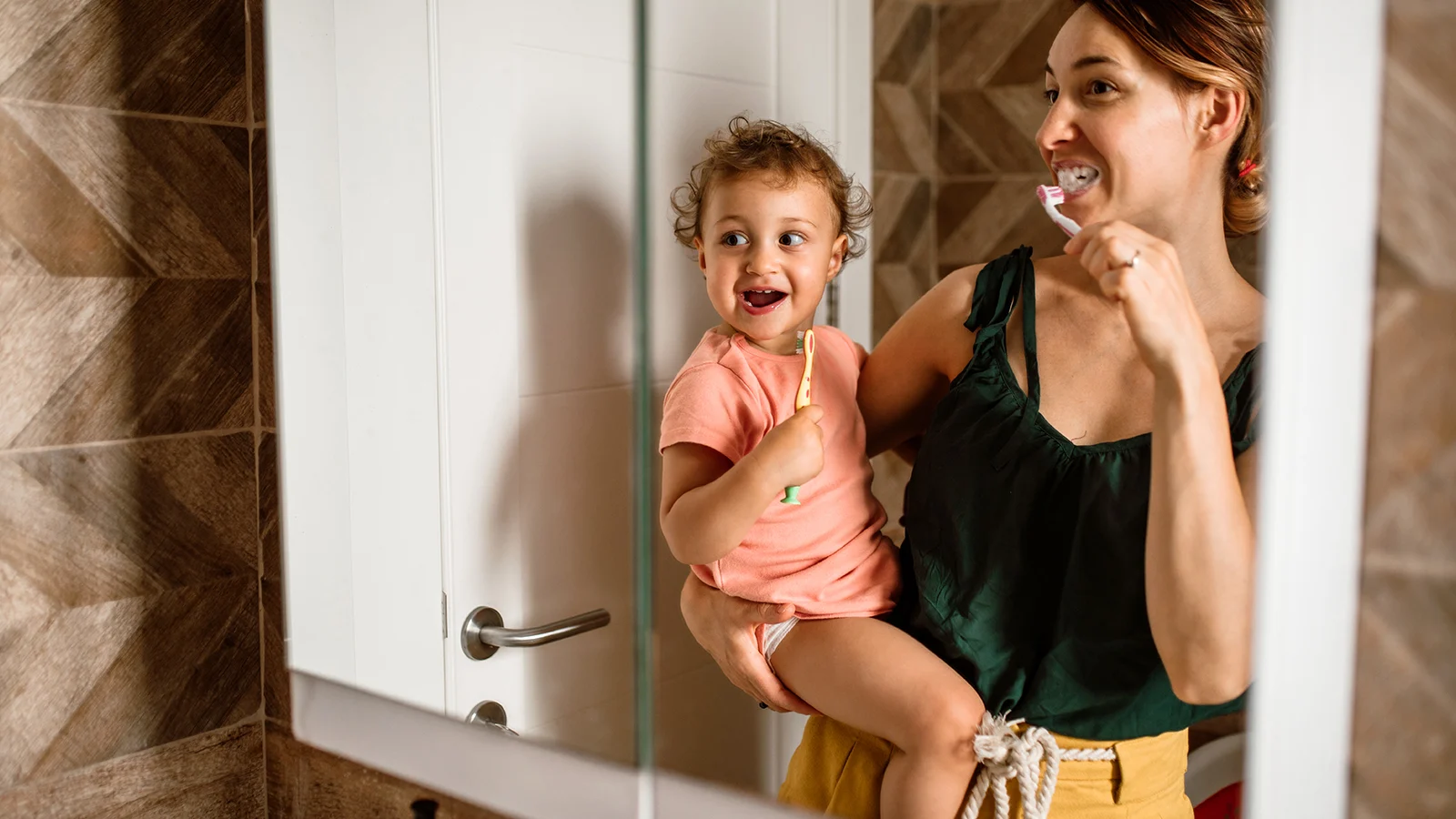 Mother holding her infant brushing their teeth