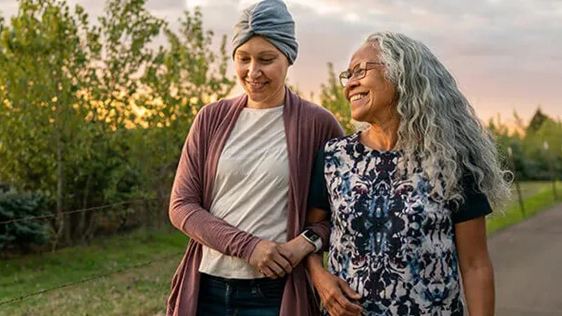 Cancer insurance - Ethnic daughter with cancer walking with her affectionate mother.