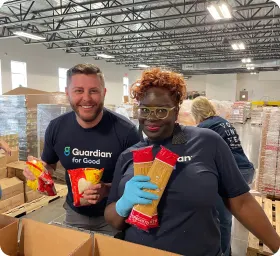 3,500+ - Two Guardian colleagues in matching t-shirts fill boxes with packaged pasta at a food pantry