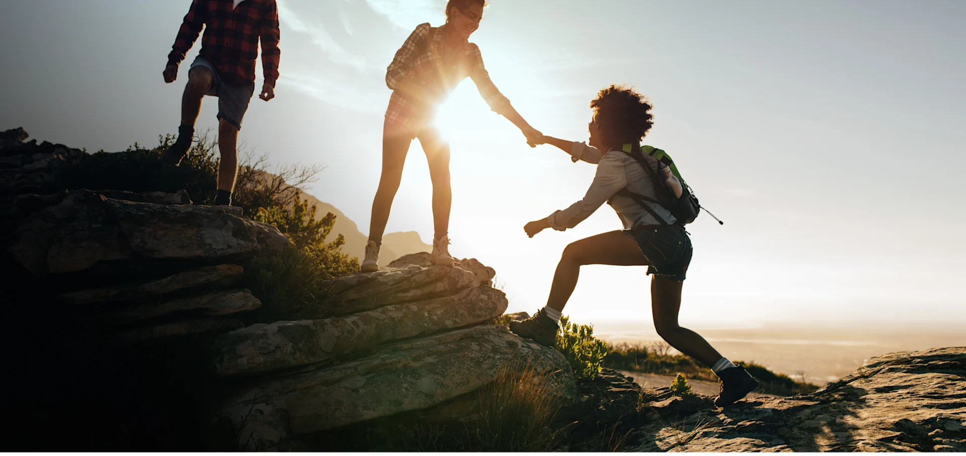 Woman helping friend to climb up the rock while hiking. Teamwork of two women hiker helping each other on top of mountain climbing.