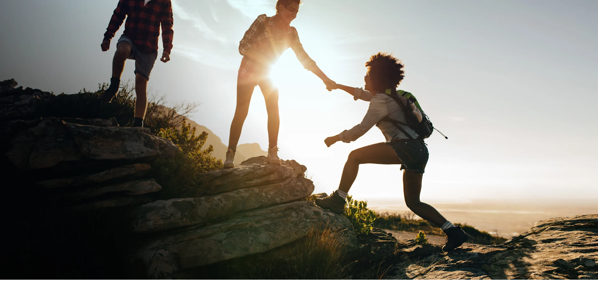 Woman helping friend to climb up the rock while hiking. Teamwork of two women hiker helping each other on top of mountain climbing.