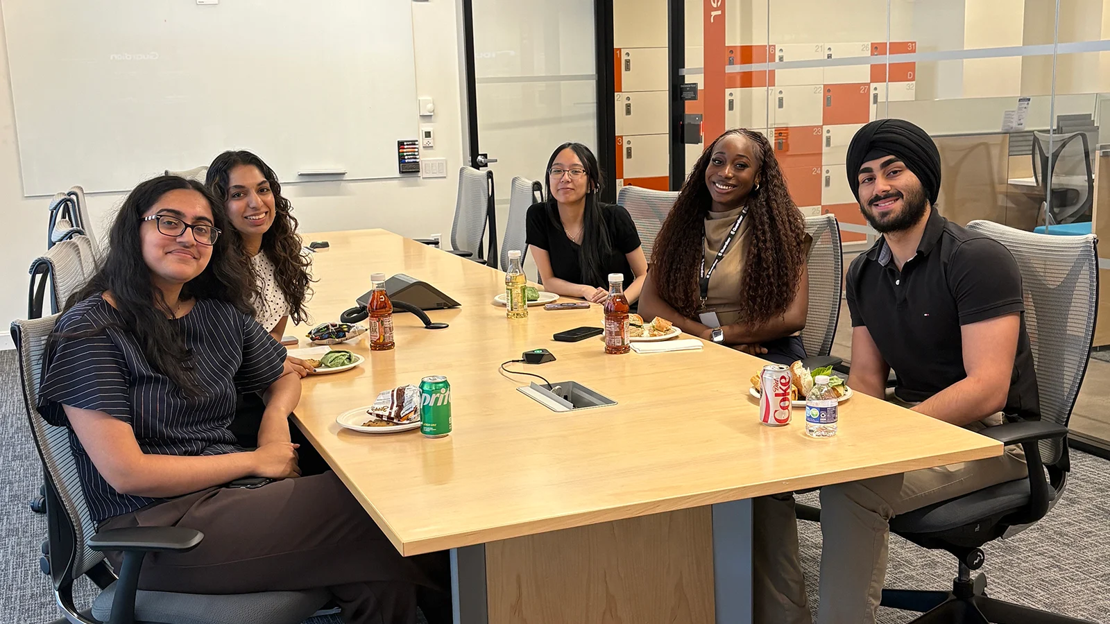 Five people sit around a conference table during a group lunch in an office.
